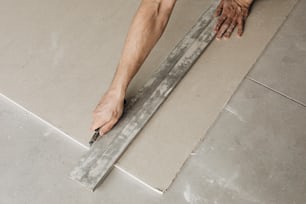 um homem colocando azulejo no chão com uma régua