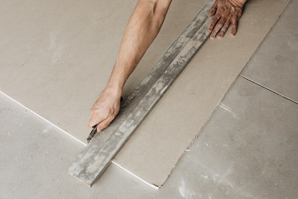 um homem colocando azulejo no chão com uma régua