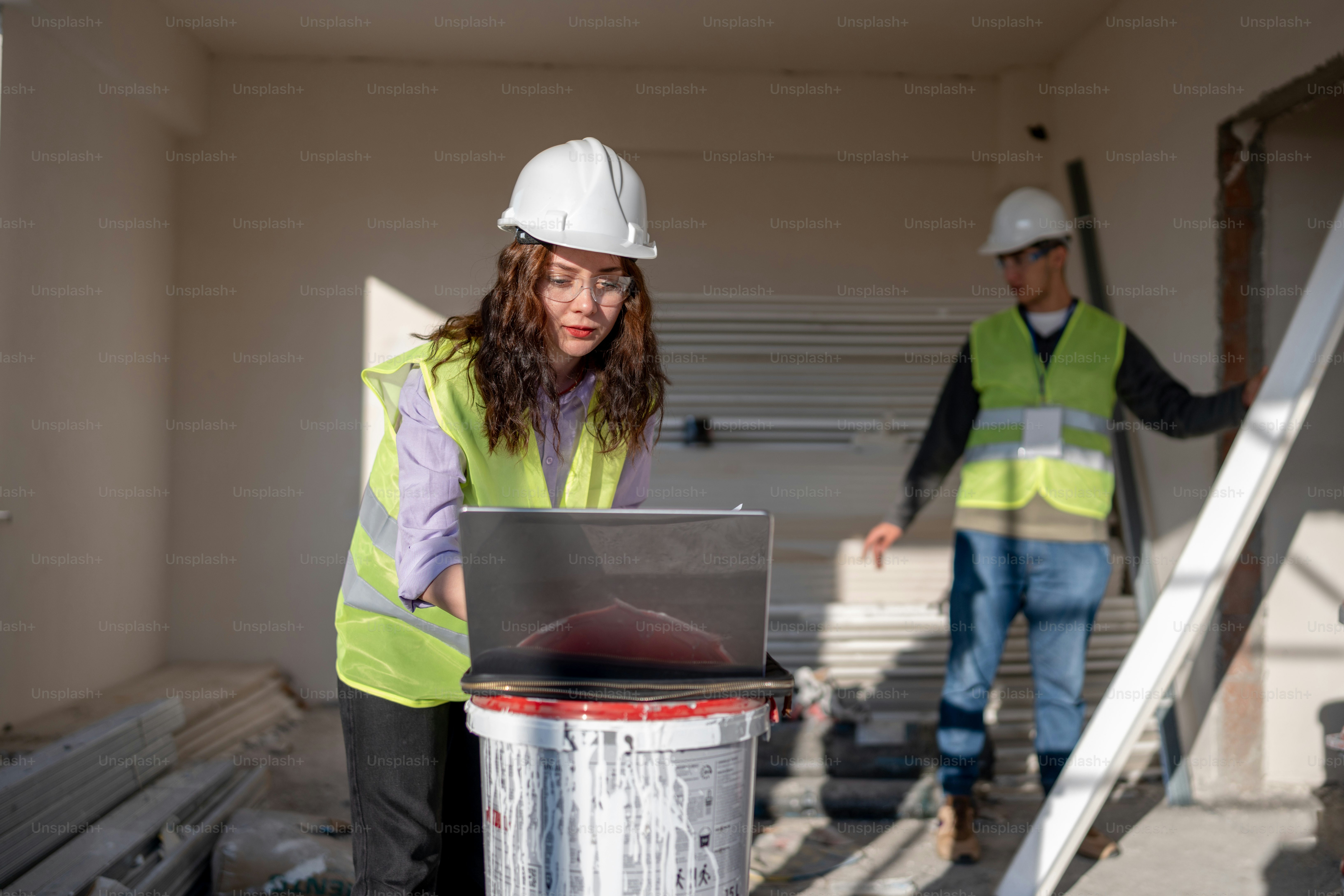 a man and a woman in safety vests working on a laptop