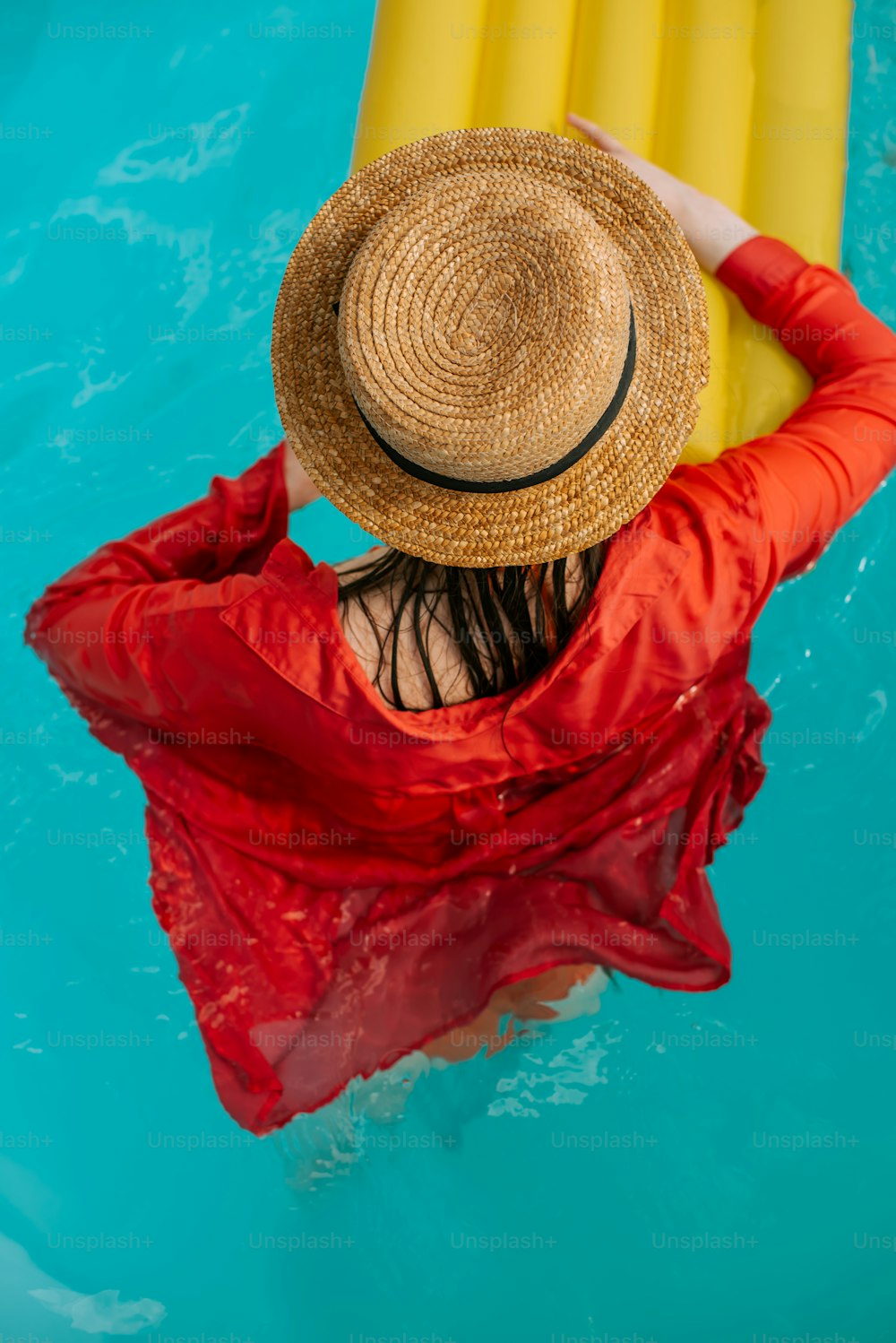 uma mulher em um vestido vermelho e um chapéu de palha em uma piscina