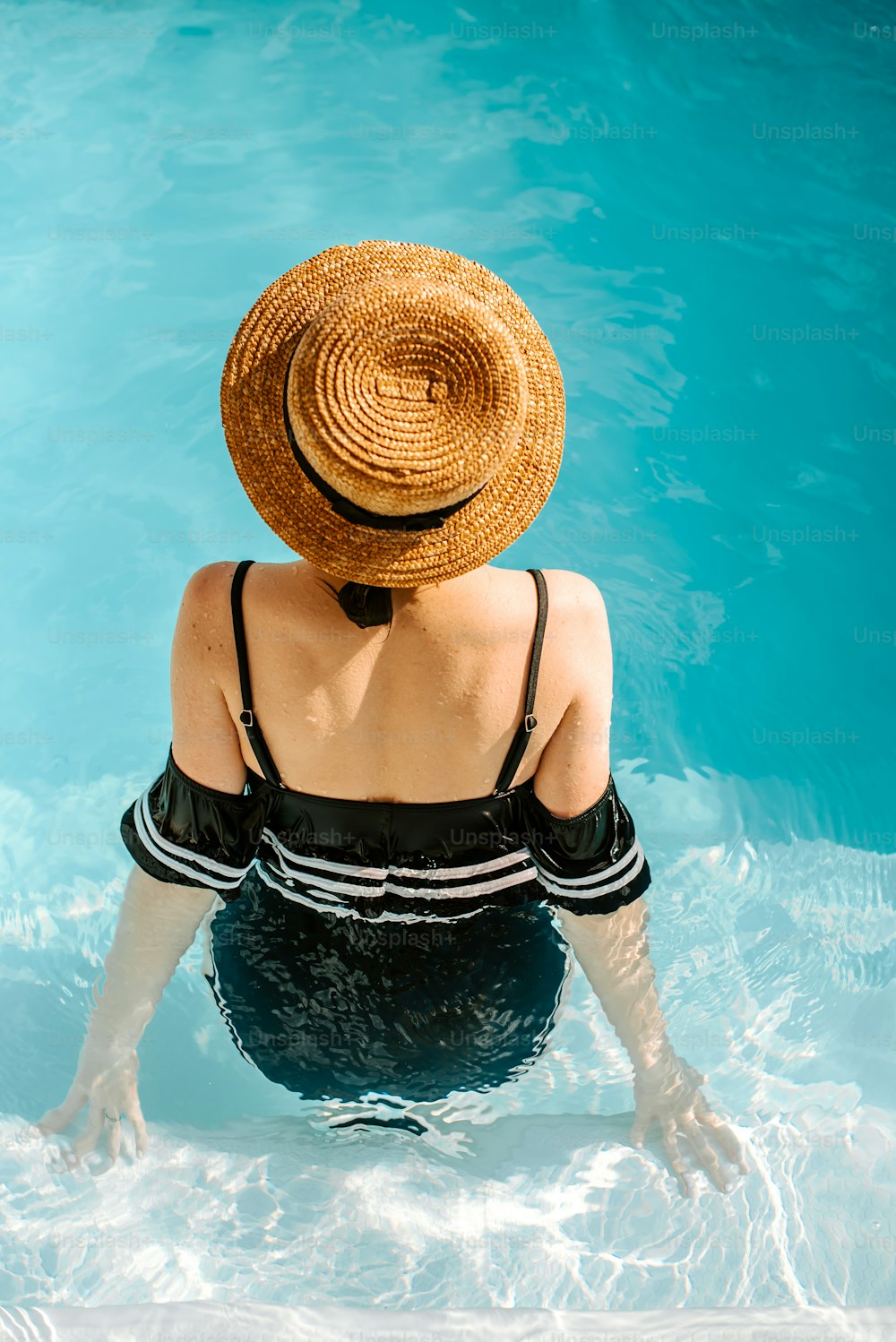 Une femme coiffée d’un chapeau de paille assise dans une piscine