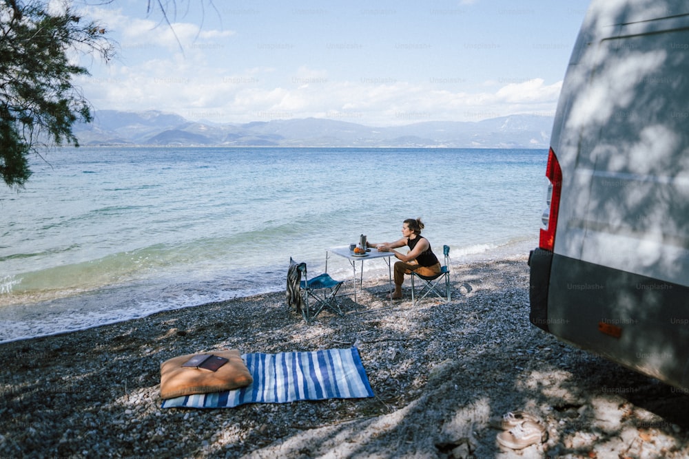 uma mulher sentada em uma praia ao lado de uma van