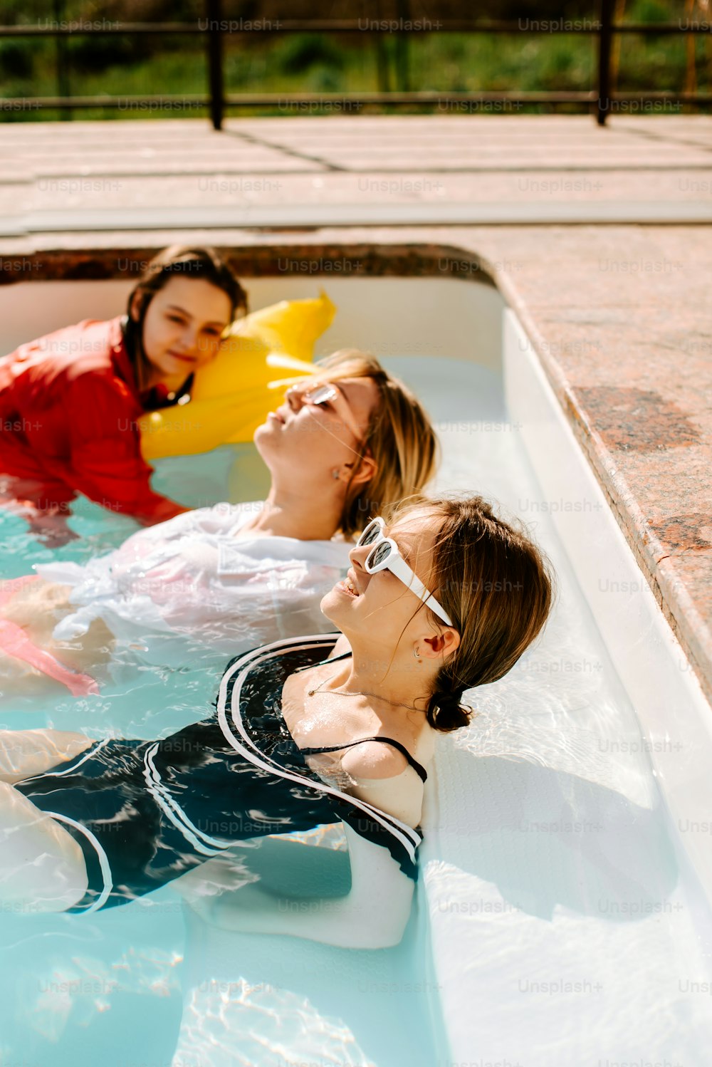 três mulheres em uma piscina com patos de borracha