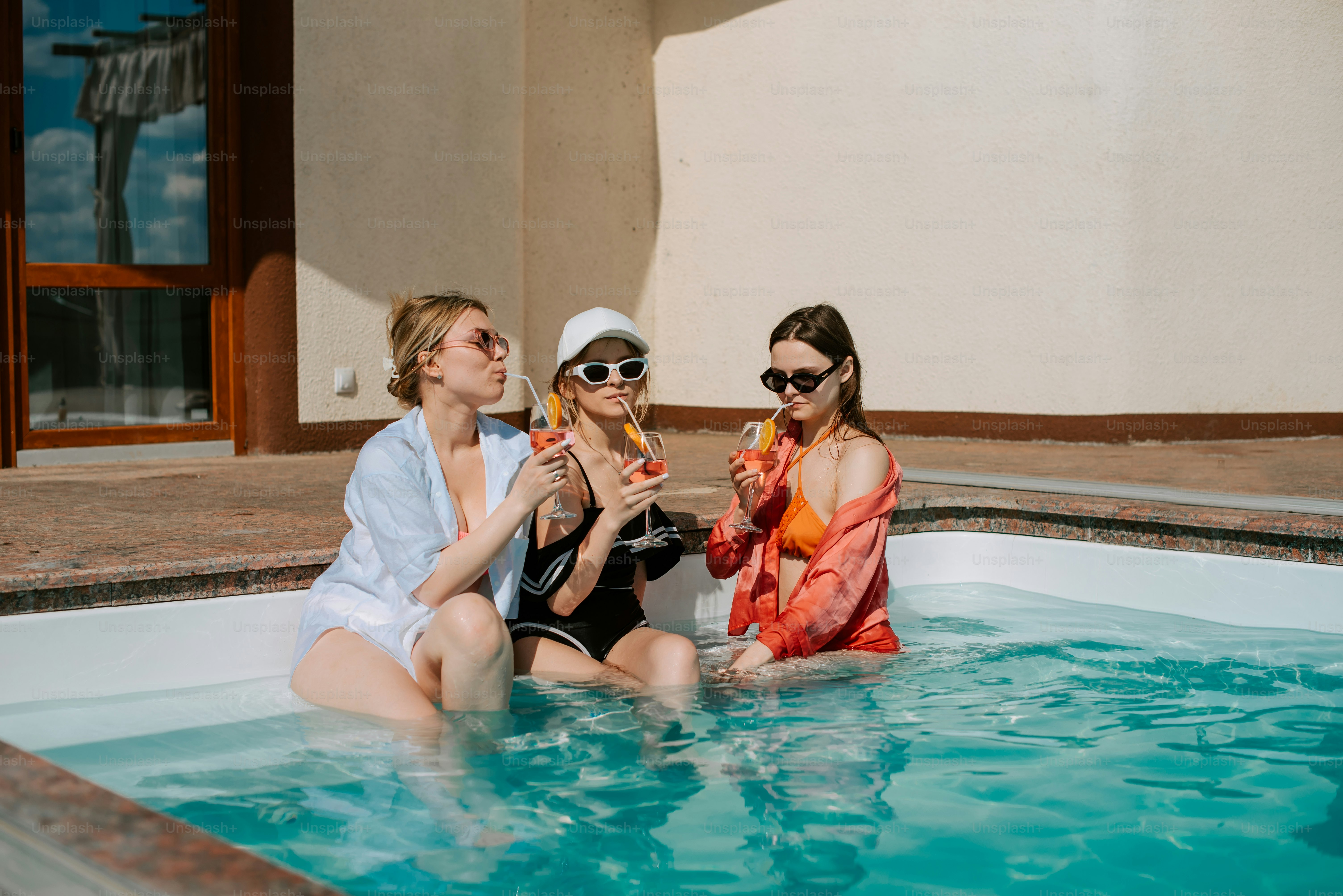 Tres mujeres sentadas en una piscina bebiendo champán