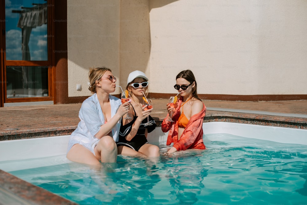 three women sitting in a pool drinking champagne