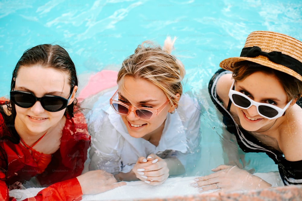 three women in sunglasses and hats in a pool