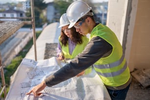 a man and a woman in safety vests are looking at a blueprint