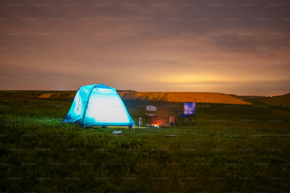 une tente bleue posée au sommet d’un champ verdoyant