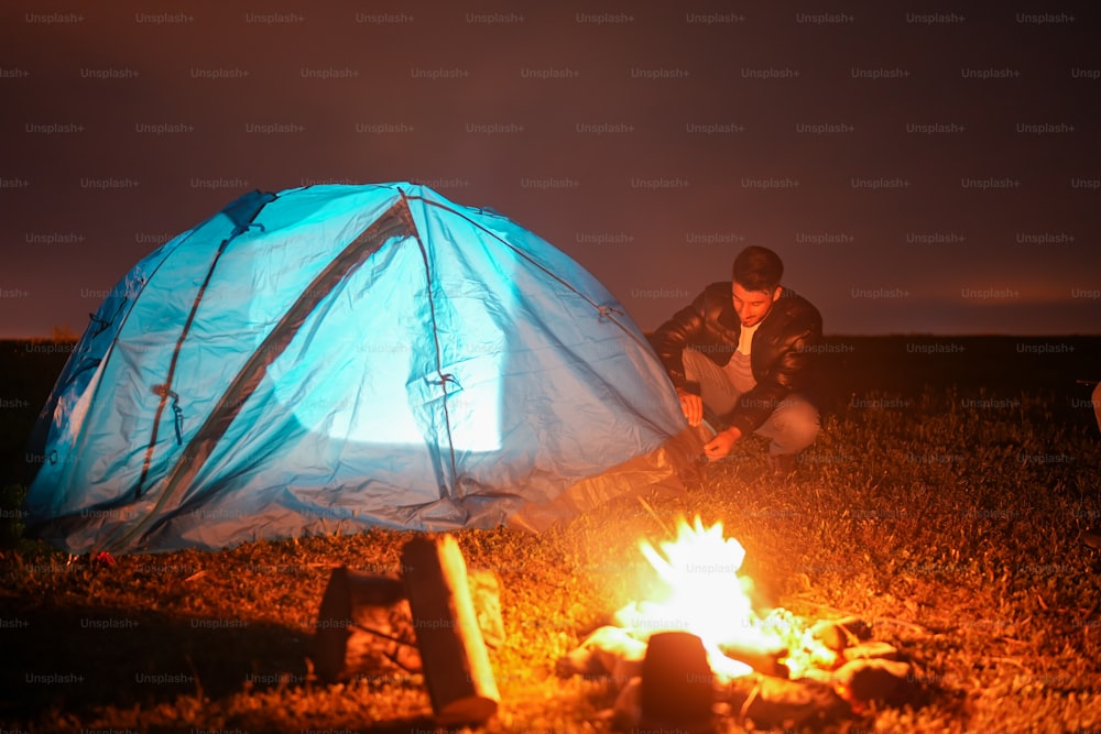 a man sitting next to a fire in a field