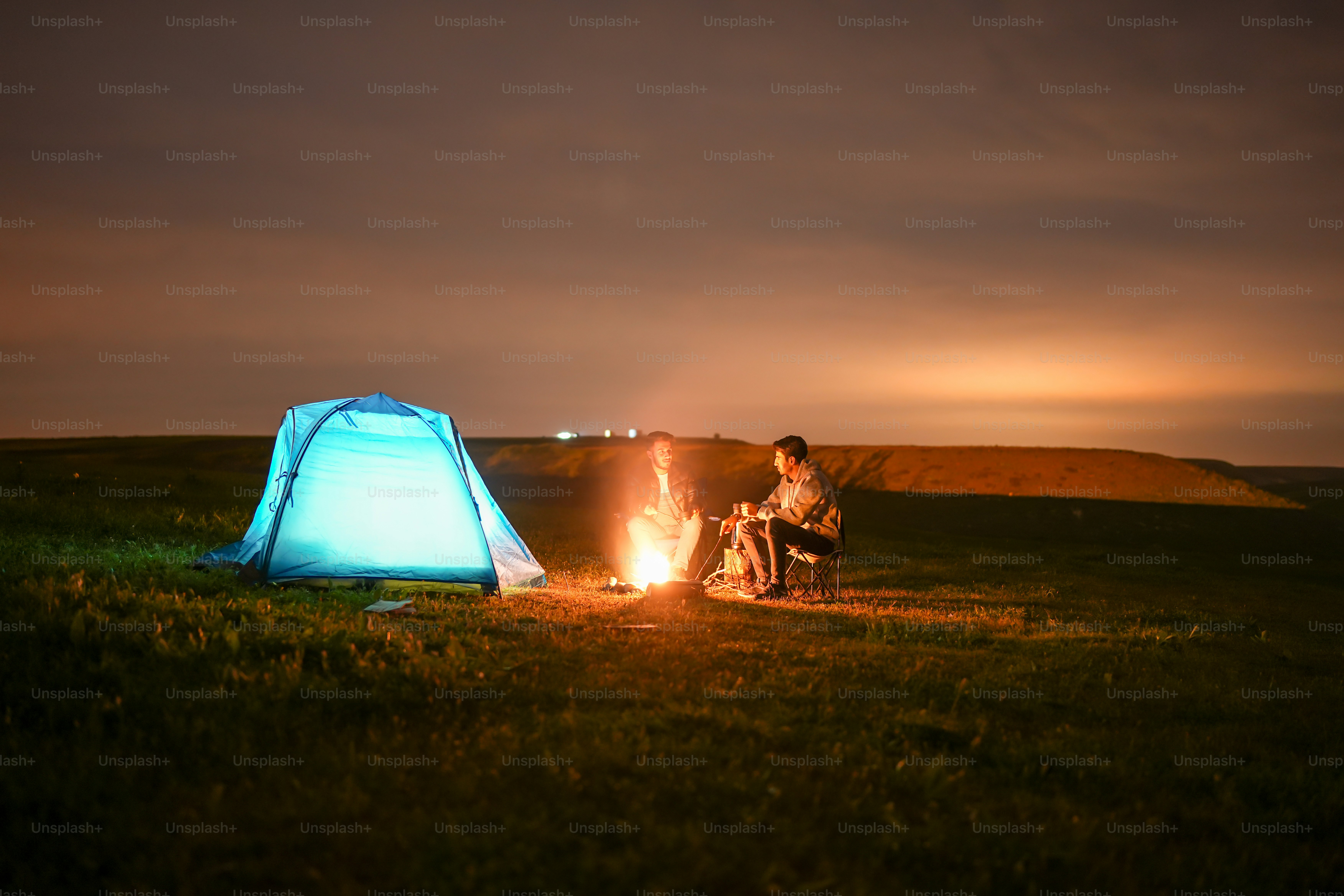 a man sitting next to a blue tent on top of a lush green field