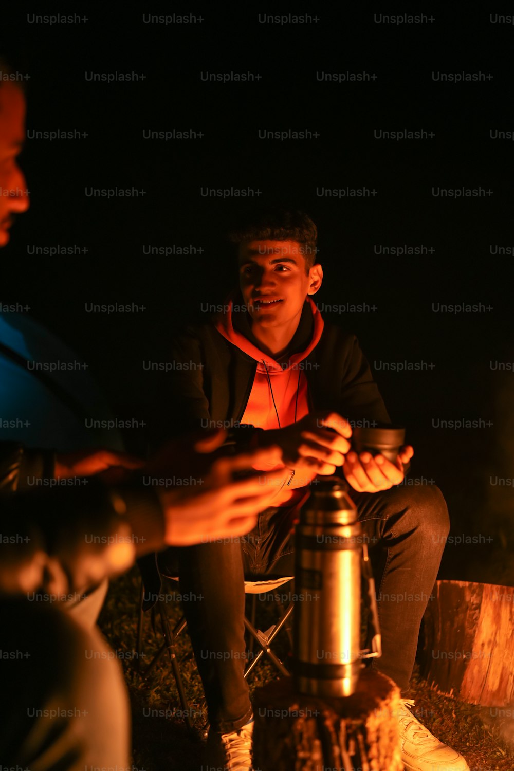 a man sitting in front of a campfire with a flashlight