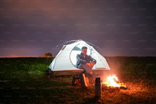 a man sitting in front of a tent next to a fire
