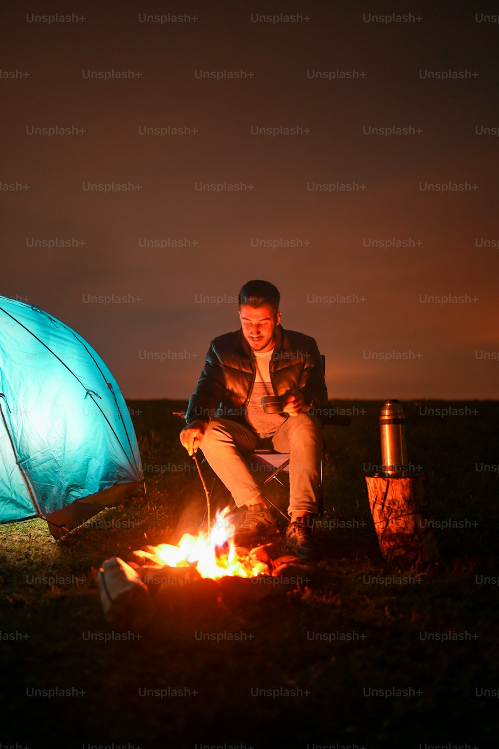 Ein Mann sitzt vor einem Lagerfeuer neben einem Zelt