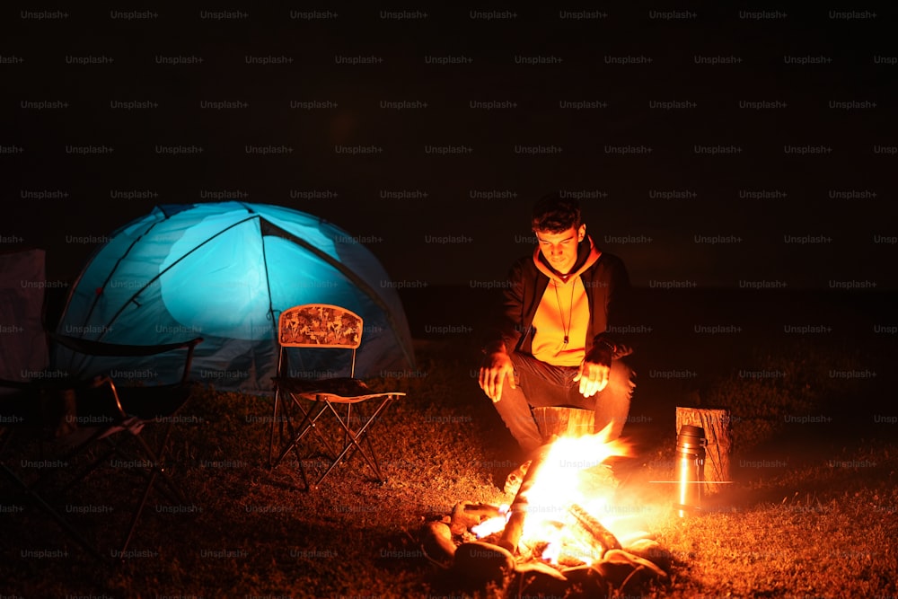 Ein Mann sitzt vor einem Lagerfeuer neben einem Zelt