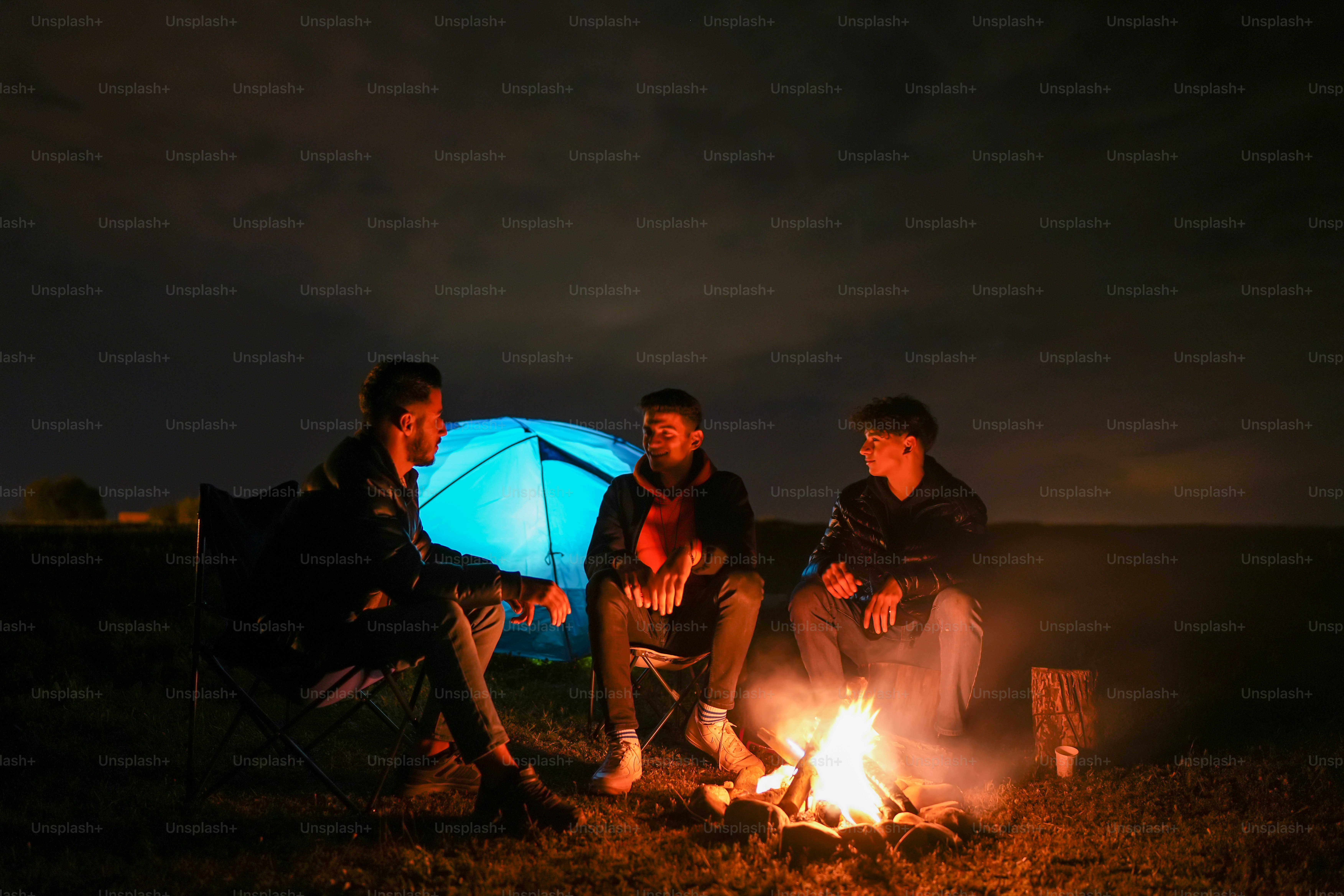 three people sitting around a campfire at night