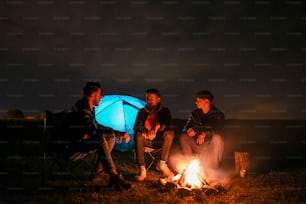 夜にキャンプファイヤーの周りに座�っている3人