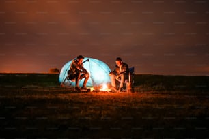 three people sitting around a campfire at night