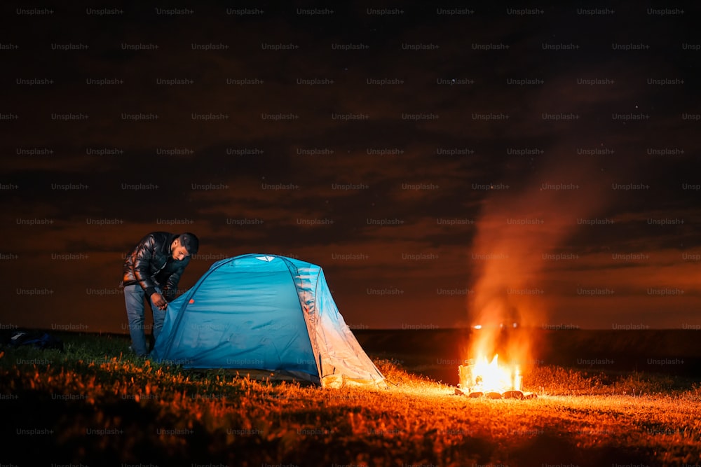 um homem ao lado de uma tenda azul em cima de um campo