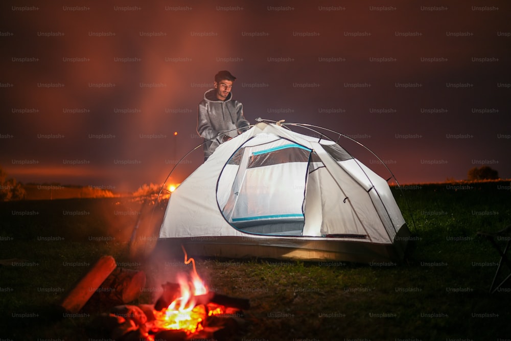 um homem sentado em cima de uma tenda ao lado de um incêndio