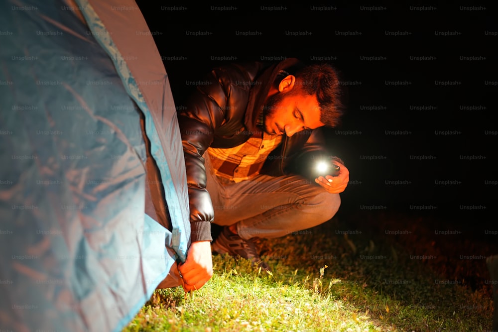 a man kneeling down next to a tent at night