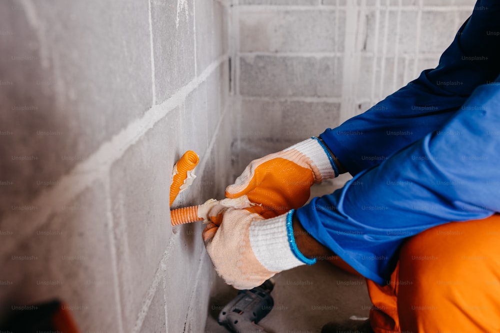 a person in orange pants and a blue jacket is putting cement on a wall