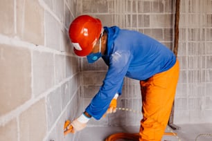 a man in orange pants and a red helmet working on a wall