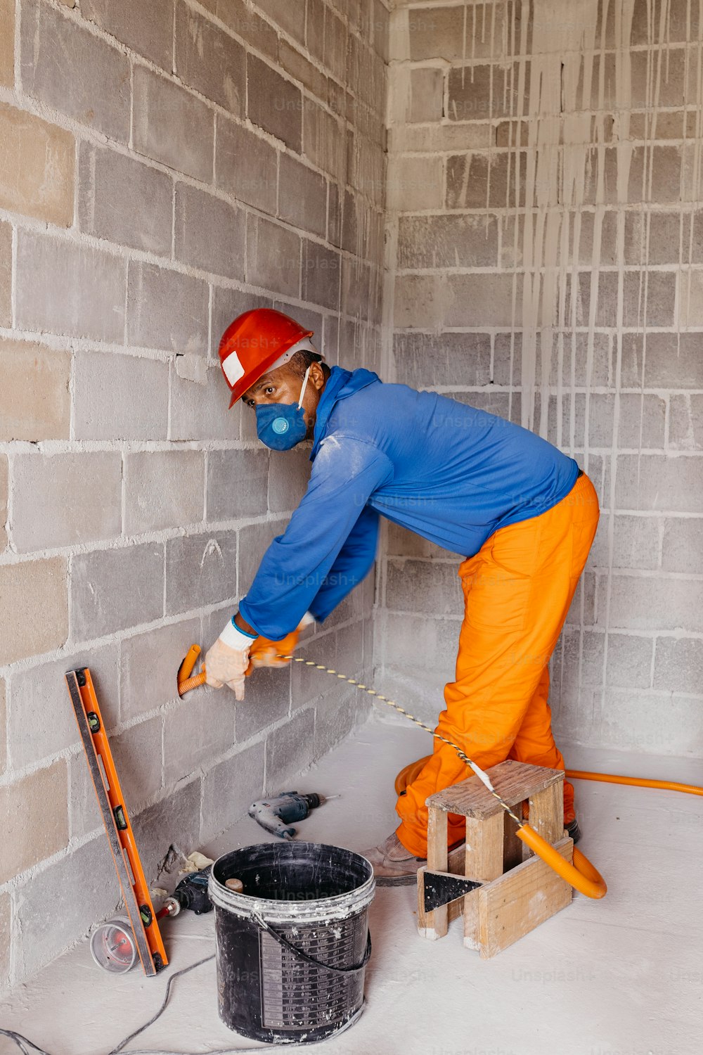 um homem de macacão azul e laranja trabalhando em uma parede de tijolos