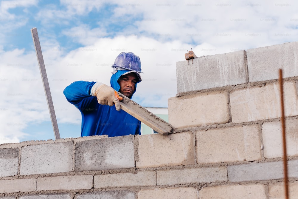 um homem usando um capacete e uma camisa azul trabalhando em uma parede de tijolos