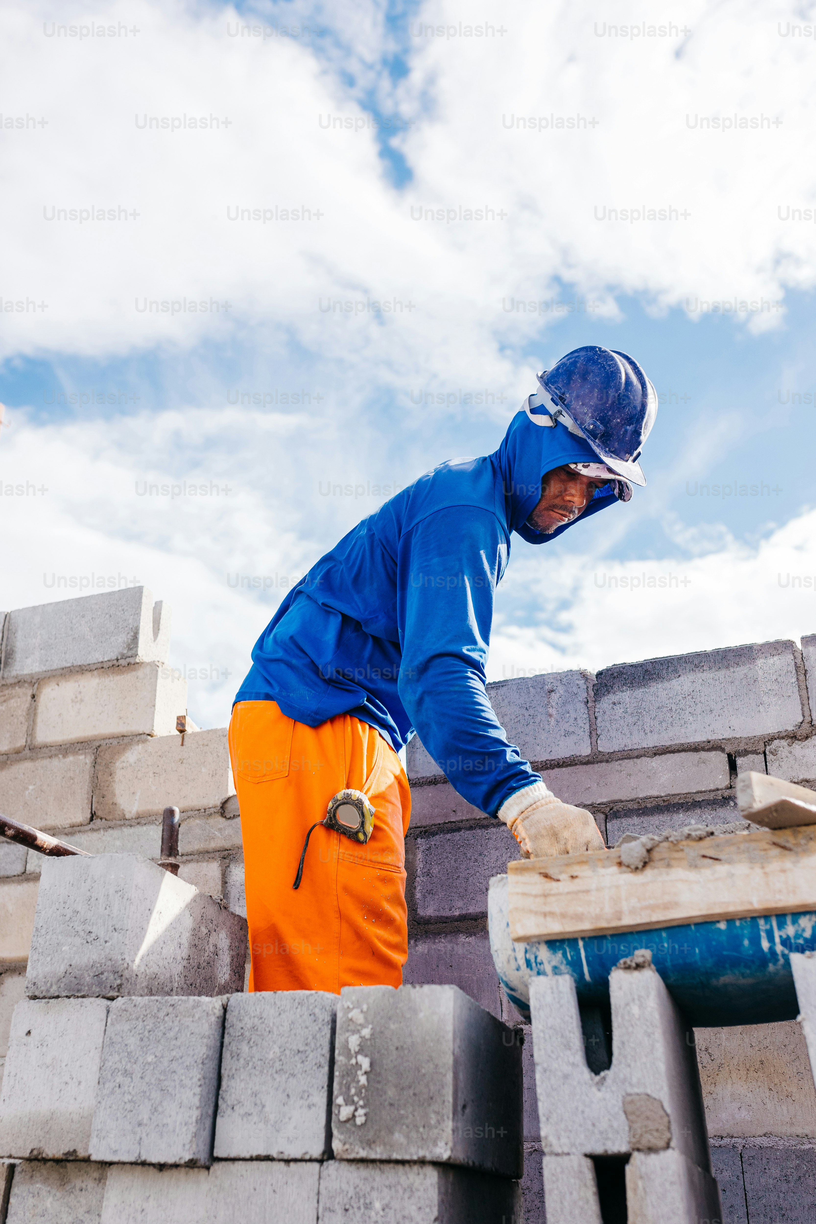 a man in a blue jacket and orange pants working on a brick wall
