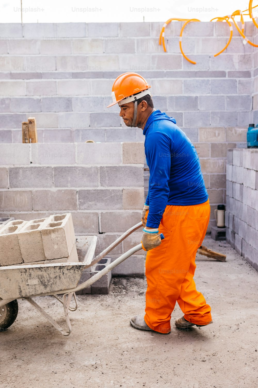 a man in orange pants and a blue shirt is pushing a wheelbarrow