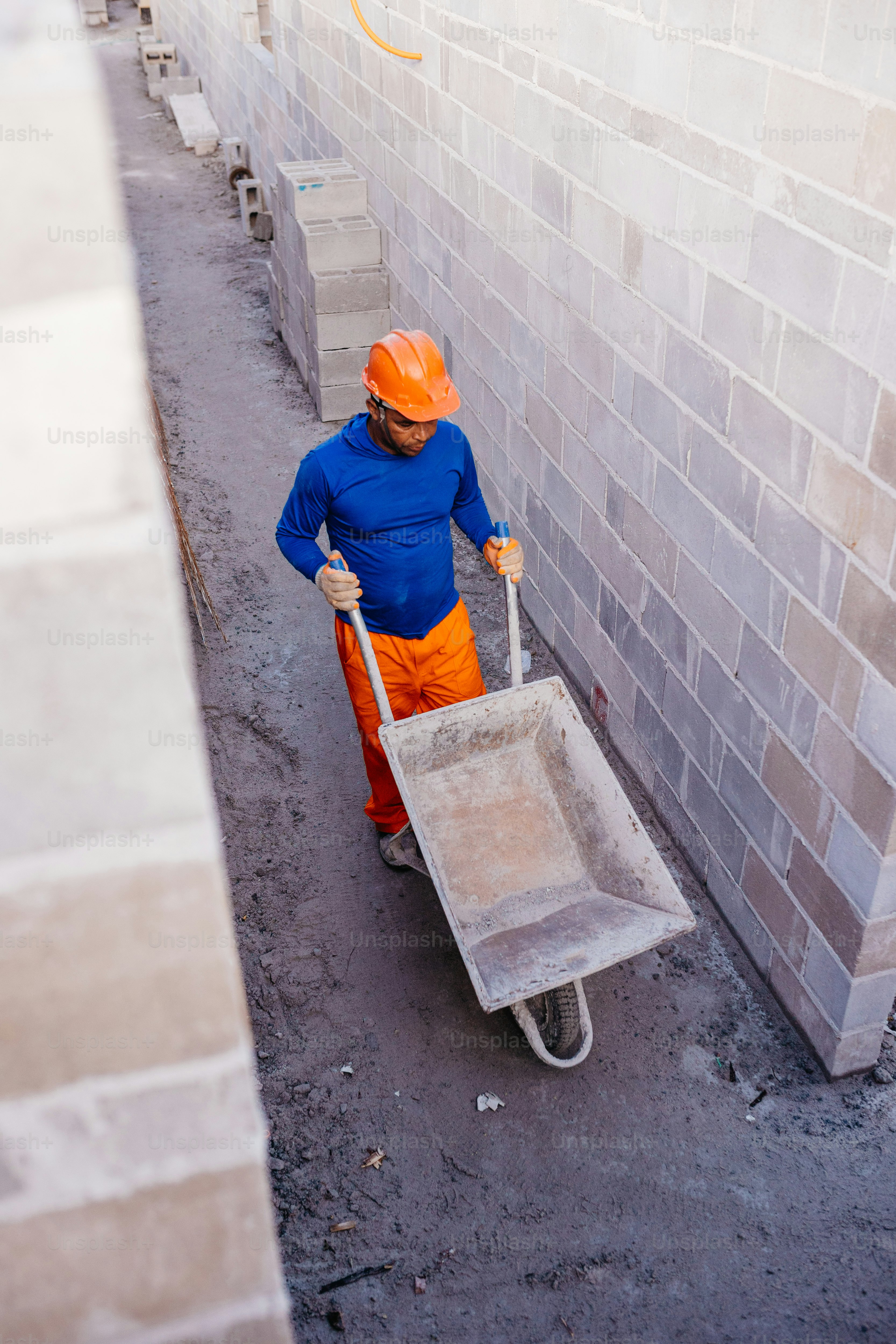 a man in orange pants and an orange helmet pushing a wheelbarrow