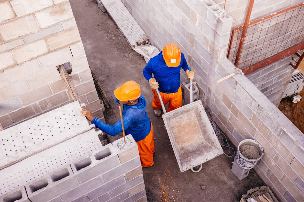 two men in orange and blue work on a construction site