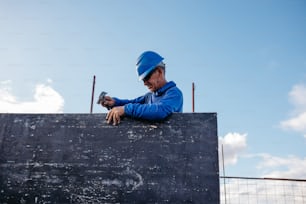 a man in a blue jacket and hard hat leaning on a wall