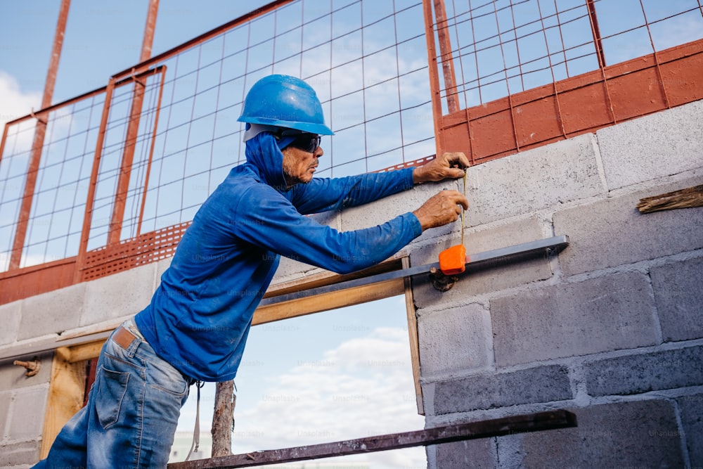 a man in a hard hat and blue jacket working on a brick wall