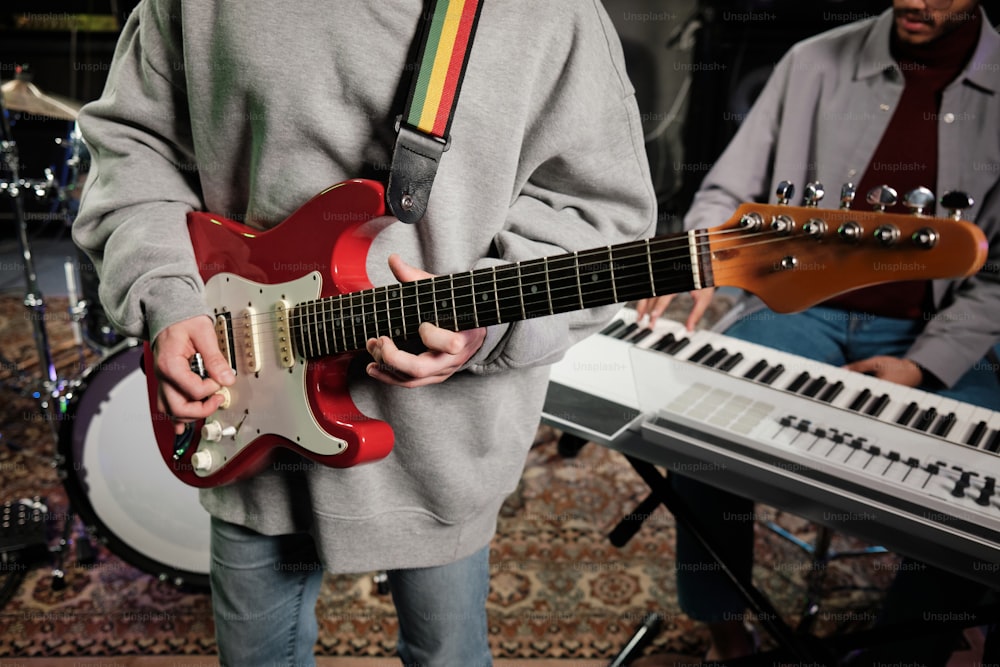 a man holding a red guitar in front of a keyboard