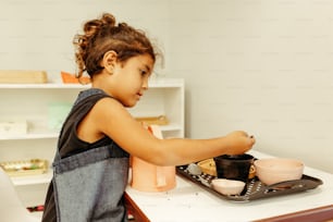 Ein kleines Mädchen, das an einem Tisch mit einem Tablett mit Essen sitzt
