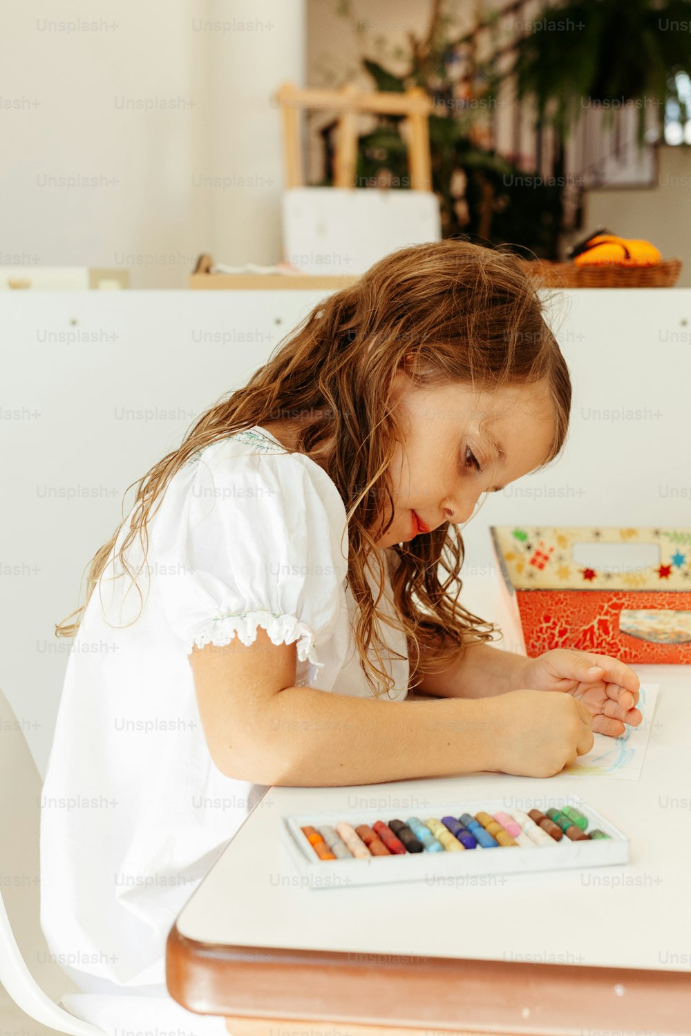 a little girl sitting at a table with a book and some crayons