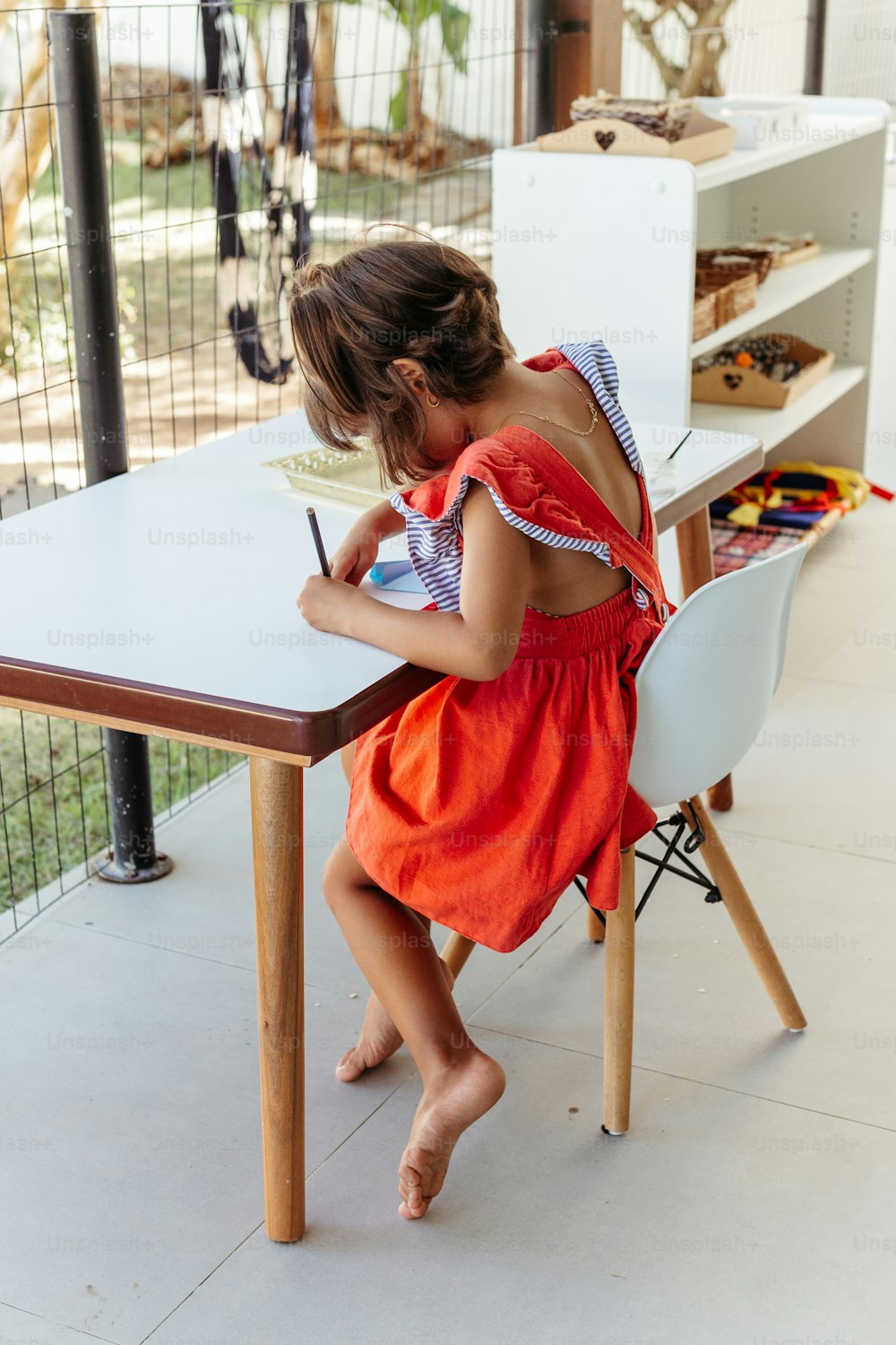 uma menina sentada em uma mesa escrevendo em um pedaço de papel