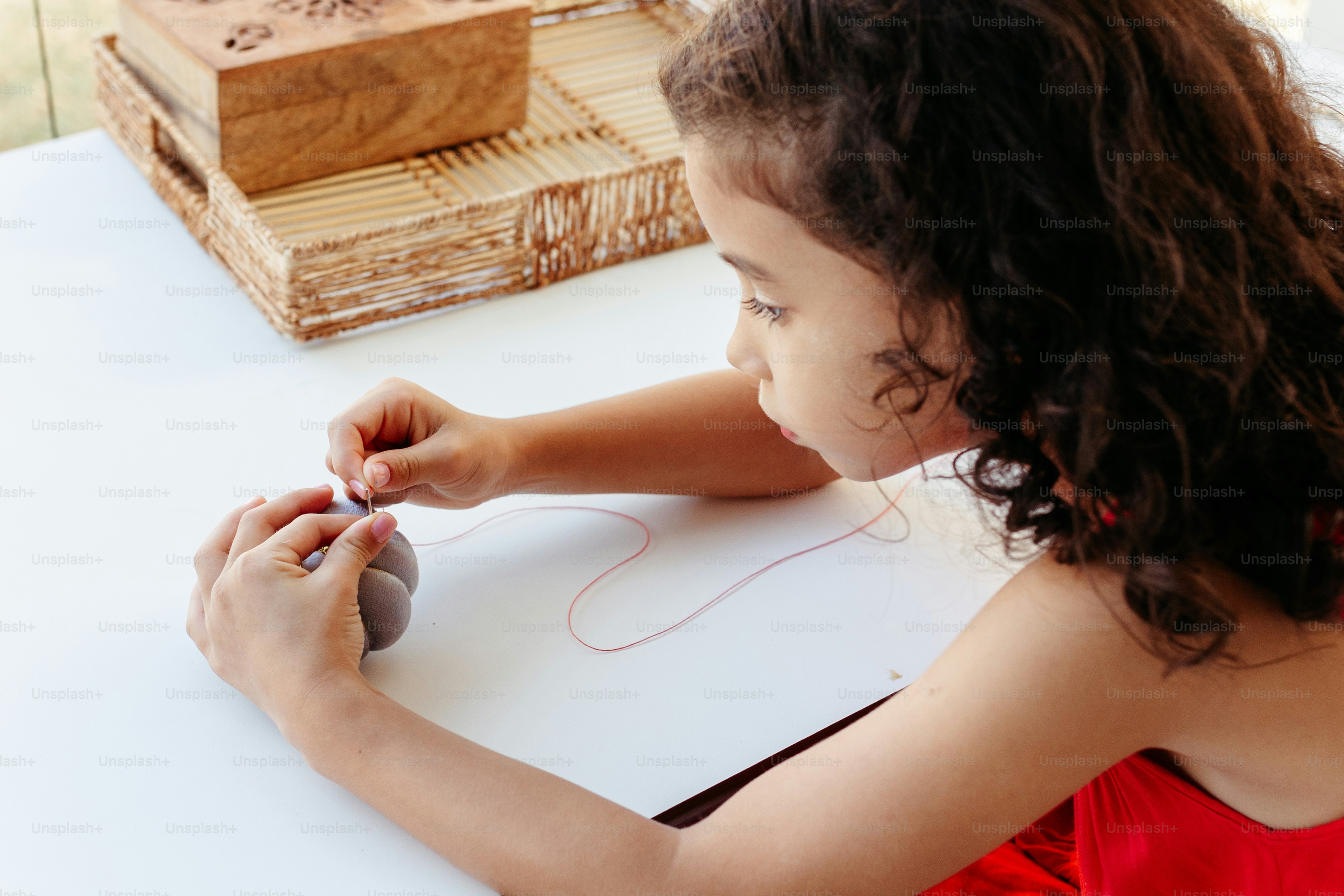 a little girl sitting at a table with a ball and thread