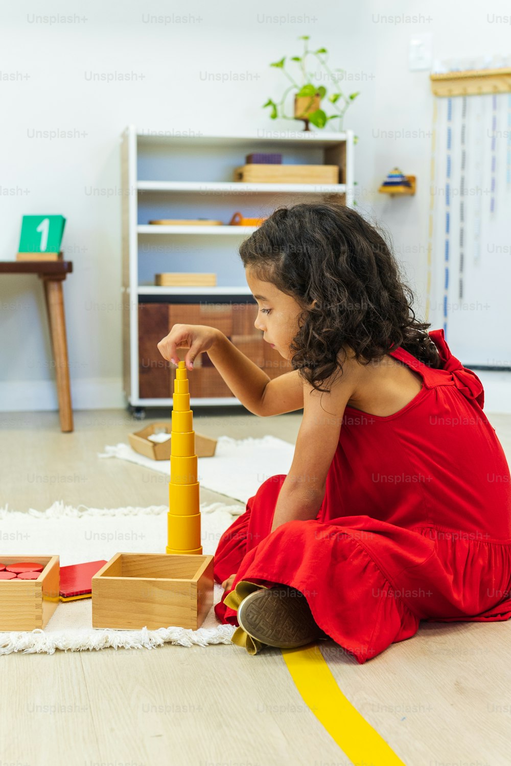 a little girl in a red dress playing with a wooden tower