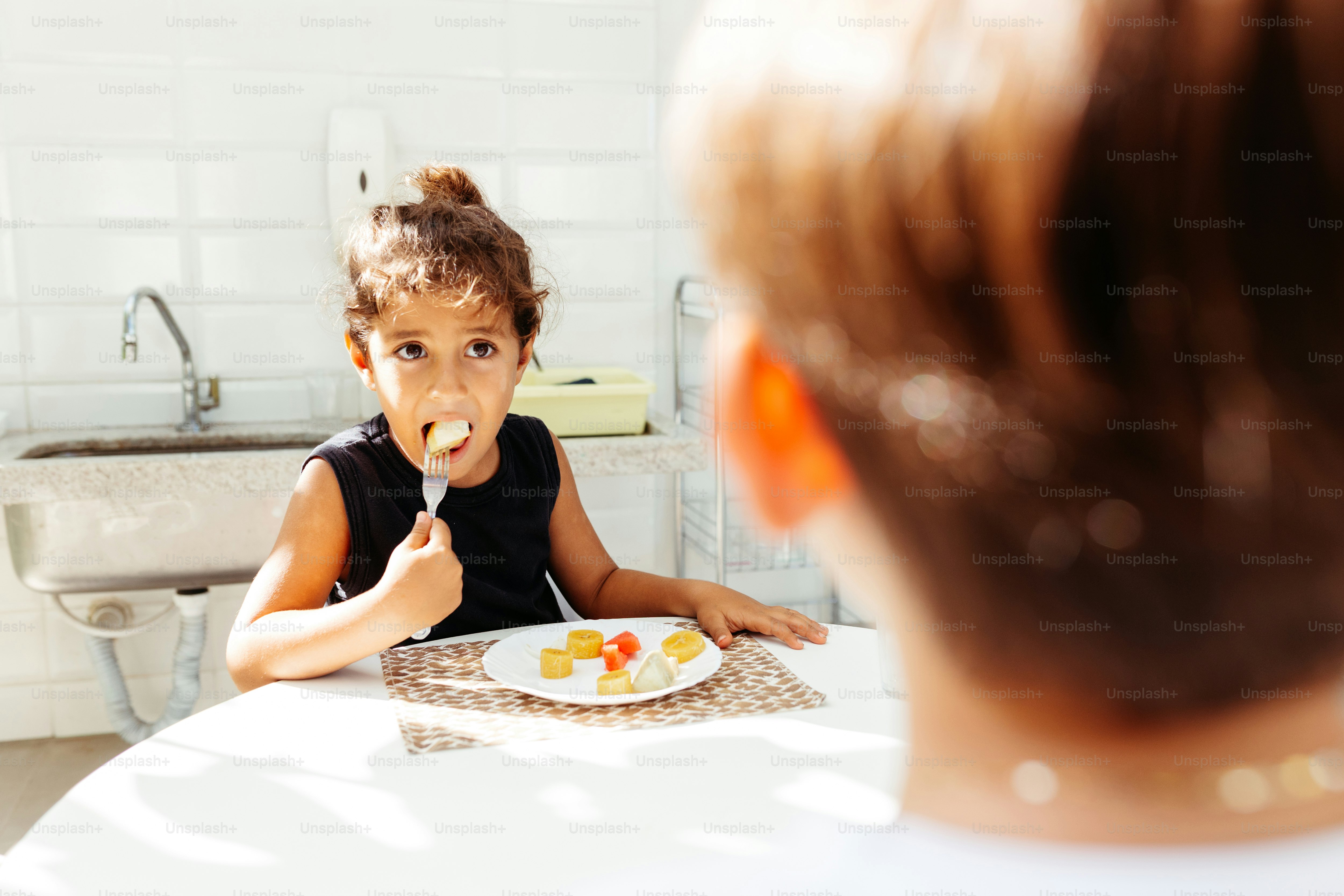 a little girl sitting at a table with a plate of food in front of her
