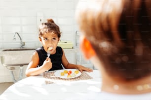 ein kleines Mädchen, das an einem Tisch sitzt und einen Teller mit Essen vor sich hat
