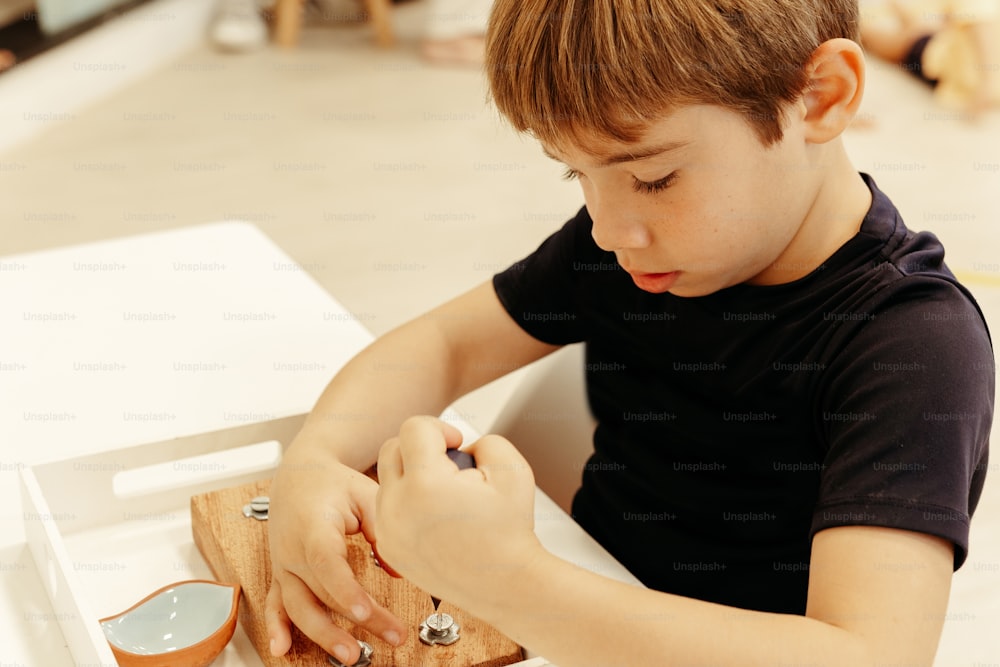 Un niño sentado en una mesa cortando un trozo de madera