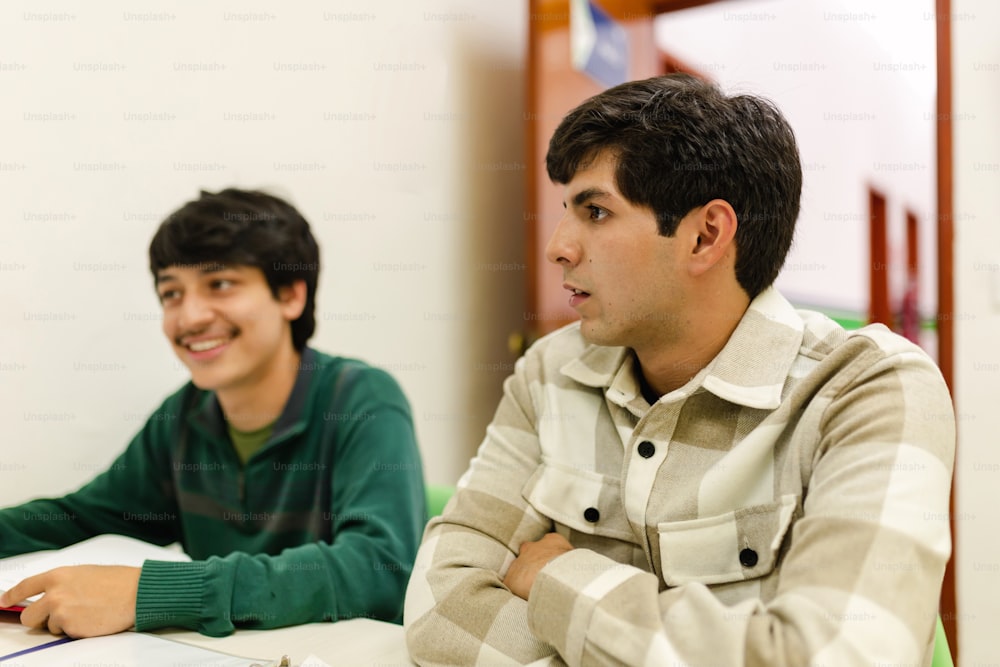 two young men sitting at a table in front of a laptop computer