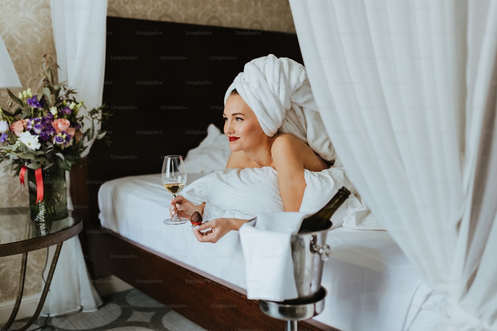 una donna seduta su un letto con in mano un bicchiere di vino