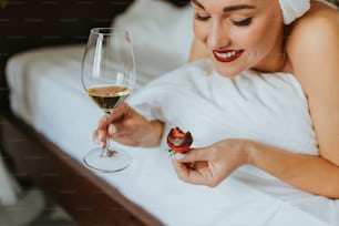 a woman laying in bed with a glass of wine and a piece of fruit