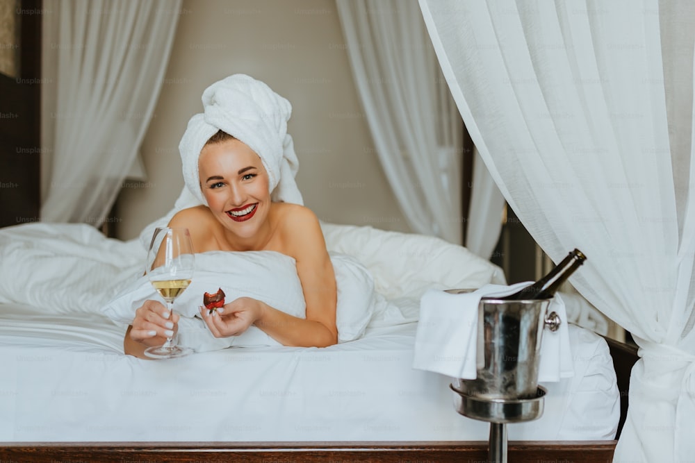 Una donna che si trova a letto con un bicchiere di vino