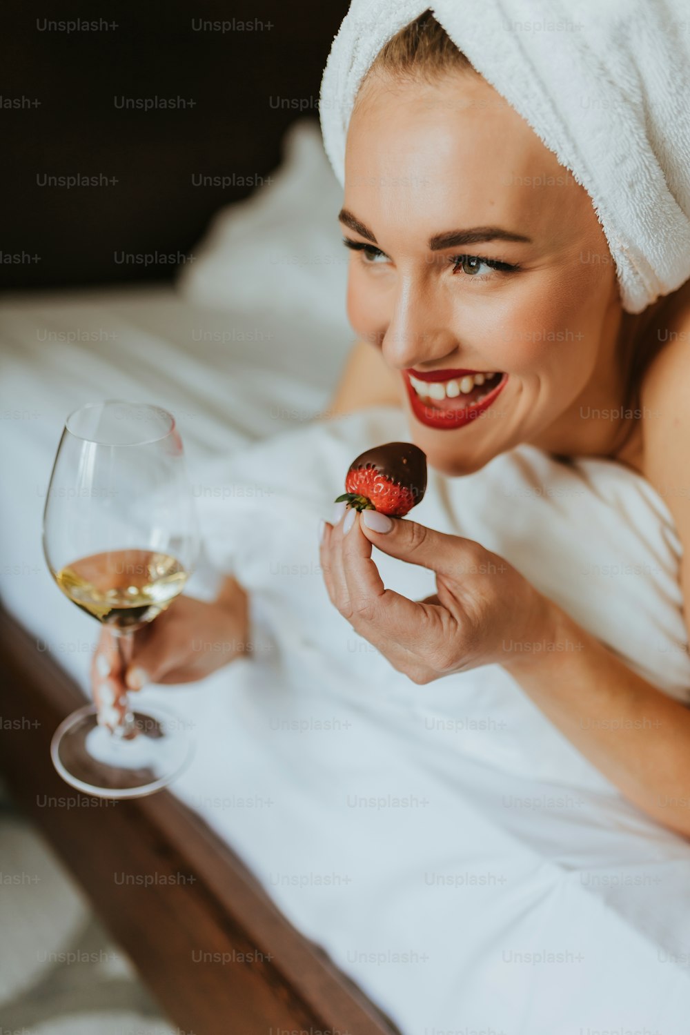 a woman with a towel on her head holding a strawberry and a glass of wine