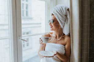 una donna in un asciugamano che tiene una tazza e un piattino