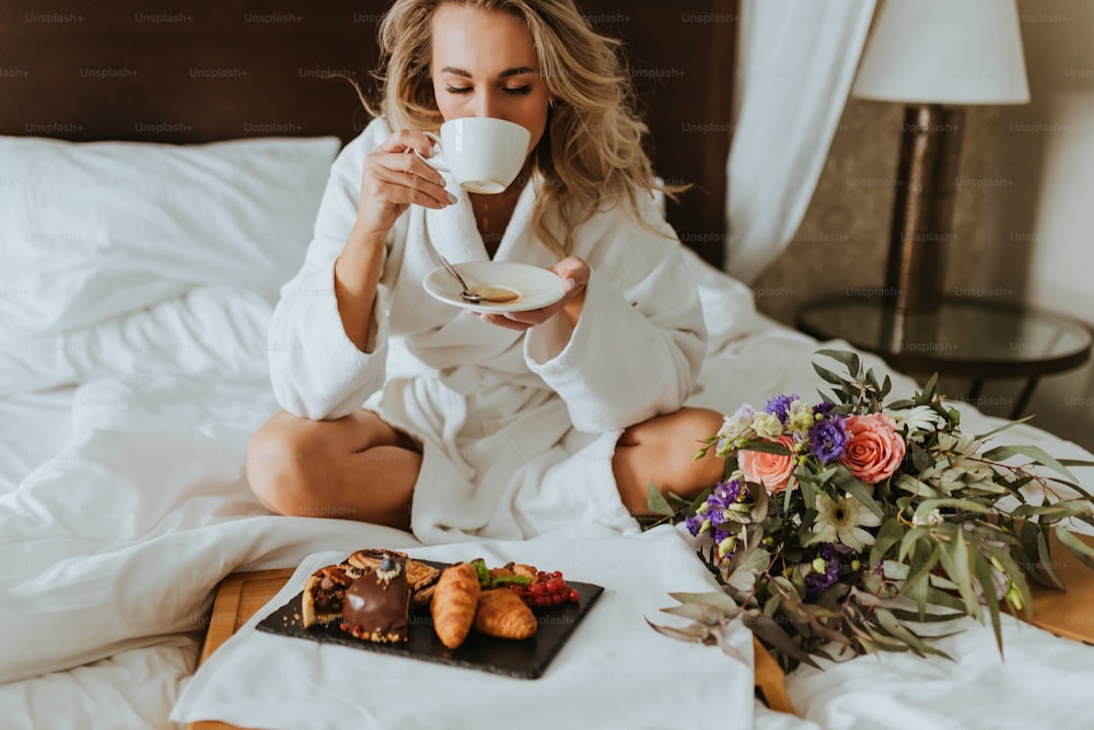 uma mulher sentada em uma cama bebendo uma xícara de café